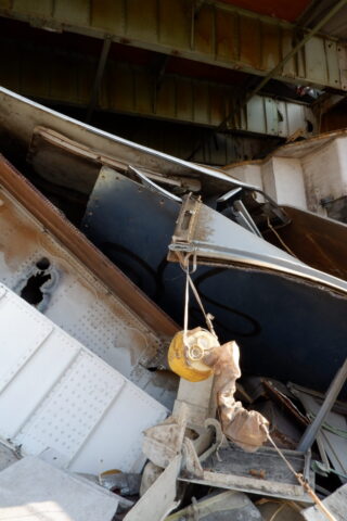 Eingestürzte Metallstruktur und Trümmer, darunter verbogene Stahlträger und eine gelbe Rolle, unter einer beschädigten Brücke oder Überführung.