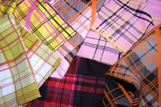 Verschiedene Stoffe mit unterschiedlichen bunten Karomustern in den Farben Rosa, Gelb, Rot, Schwarz und Orange, die übereinander angeordnet sind.