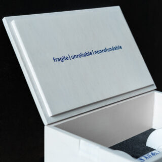 Eine weiße Schachtel mit den Worten „zerbrechlich | unzuverlässig | nicht erstattungsfähig“ in blauer Schrift auf der Innenseite des Deckels.