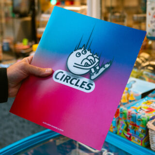 Eine Person hält in einem Geschäft mit Spielzeug im Hintergrund einen bunten Ordner mit Farbverlaufsdesign und dem Wort „KREISE“ unter einer Cartoon-Grafik.