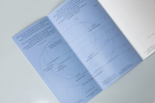 Ein blaues Heft ist auf einer Seite aufgeschlagen, auf der sich Kreise, Tabellen und Text in minimalistischer Schriftart auf einer weißen Oberfläche überlappen.