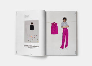 Eine aufgeschlagene Zeitschrift zeigt auf der linken Seite das Porträt einer Person in schwarzem Outfit und auf der rechten Seite dieselbe Person mit lila Weste und rosa Hose.