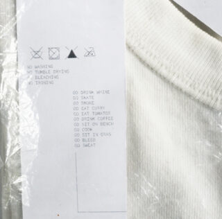 Ein weißes Kleidungsstück mit einem Pflegeetikett mit Wäschesymbolen, Hinweisen zum Nichtwaschen, Trocknen im Trockner, Bleichen oder Bügeln und einer Liste mit unkonventionellen Vorschlägen wie „GEH WEIN TRINKEN“ und „GEH SKATEN“.