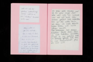 Eine offene rosa Grußkarte mit handgeschriebenen Nachrichten in deutscher Sprache auf beiden Seiten, die jeweils auf separate weiße Papierstücke geschrieben und auf die Karte geklebt sind.