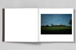 Auf einer Seite des Fotobuchs ist eine weite Wiese mit einem großen Gebäude und Bäumen in der Ferne unter einem blauen Himmel aufgeschlagen.