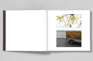 Ein verrostetes Fahrzeug mit brauner Abdeckung steht neben einem weißen Zelt unter einem Baum mit gelben Blättern.