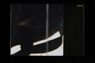 Ein dunkles, abstraktes Bild mit weißen Lichtstreifen und einer sichtbaren Seitenfalte in der Mitte; in der oberen rechten Ecke erscheint ein gelber Zeitstempel „00:27:05“.