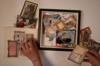 Zwei Hände sortieren eine Sammlung kleiner gerahmter Bilder und Kunstwerke, von denen sich einige in einer Schachtel befinden und einige auf einem Tisch ausgebreitet sind.