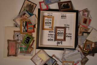 Eine Sammlung kleiner gerahmter Bilder, Papiere und Objekte, die um einen zentralen Rahmen angeordnet sind und einen deutschen Text mit Fragen zu Rahmen und Kunst enthalten.