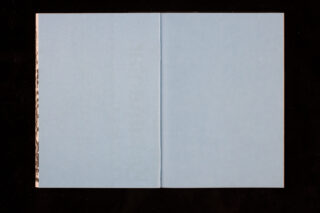 Ein offenes Buch liegt flach und zeigt zwei leere hellblaue Seiten auf schwarzem Hintergrund.