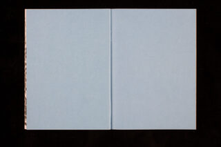 Ein offenes Buch zeigt zwei leere hellblaue Seiten vor einem schwarzen Hintergrund.