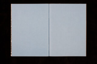 Ein aufgeschlagenes Buch mit zwei leeren hellblauen Seiten vor einem schwarzen Hintergrund.