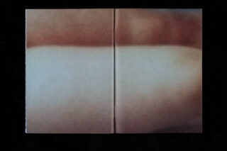 Ein verschwommenes, abstraktes Bild mit sanften Braun-, Pfirsich- und Weißtönen auf einem offenen Buch vor einem schwarzen Hintergrund.