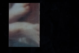 Ein verschwommenes Nahaufnahmebild von scheinbar menschlichen Zehen und Füßen ist auf einem schwarzen Hintergrund zentriert.