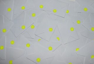 Ein Stapel weißer Umschläge, jeder mit einem runden gelben Aufkleber verschlossen, ausgebreitet und einander überlappend.