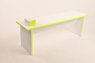Ein minimalistischer weißer Schreibtisch mit neongelben Kanten und einem kleinen weißen Würfel mit einem gelben Punkt darauf, der an einer Ecke platziert ist.