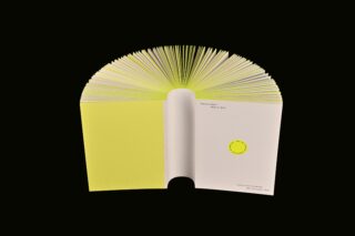 Ein offenes Buch mit leuchtend gelben, halbkreisförmig aufgefächerten Seiten vor einem schwarzen Hintergrund.