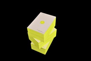 Ein Stapel aus drei dicken Büchern mit weißem Einband und neongelbem Rand, versetzt angeordnet vor schwarzem Hintergrund.