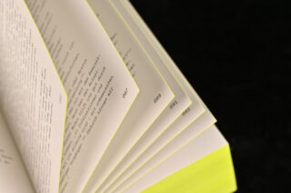 Nahaufnahme eines Buches mit mehreren leicht aufgefächerten Seiten und gelb hervorgehobenen Kanten, wobei auf den Seiten schwarzer Text sichtbar ist.