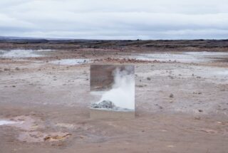 In einer kargen, geothermischen Landschaft steht ein Spiegel, der den aus einer Öffnung aufsteigenden Dampf reflektiert und sich unter einem bewölkten Himmel in die Umgebung einfügt.