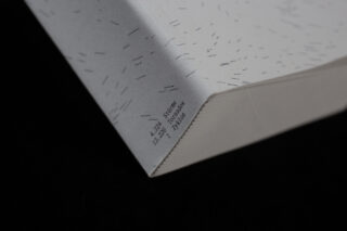 Nahaufnahme der Ecke eines Buches mit klein gedrucktem Text und kurzen schwarzen Linien auf einem weißen Einband vor einem schwarzen Hintergrund.