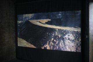 Auf einer dunklen Wand wird das Bild einer zerklüfteten Landschaft mit unbefestigten Straßen und felsigem Gelände projiziert.