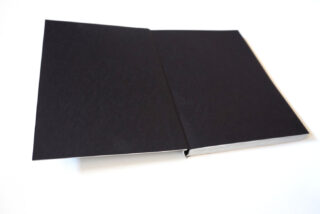 Auf einer weißen Fläche liegt ein aufgeschlagenes Buch mit schwarzen, leeren Seiten.