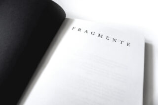 Ein offenes Buch, auf dem oben eine Seite mit dem Wort „FRAGMENTE“ in großen, weit auseinander stehenden Großbuchstaben zu sehen ist.