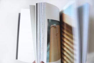 Eine Person blättert durch die Seiten eines offenen Buches oder einer Zeitschrift. Auf dem Papier sind verschwommene Bilder und Fotos auf Hochglanzpapier zu sehen.