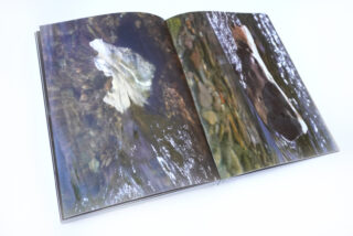 Offenes Buch mit Fotografien von Objekten unter Wasser; die linke Seite zeigt ein weißes, durchscheinendes Objekt, die rechte Seite ein dunkles, teilweise im Wasser versunkenes Objekt.