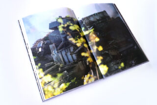 Offenes Buch mit einem Foto einer Szene im Freien mit Metalltrümmern und verschwommenem gelbgrünem Laub im Vordergrund.