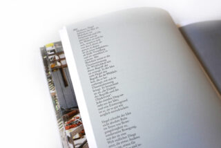 Eine Nahaufnahme eines offenen Buches, in der eine einzelne Spalte deutschen Text auf einer hellgrauen Seite zu sehen ist, mit einer weiteren, teilweise sichtbaren Seite darunter.