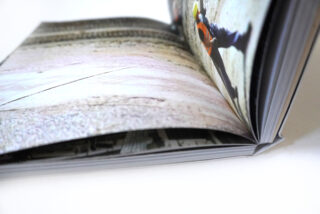 Nahaufnahme eines offenen Buches mit Hochglanzseiten, das ein verschwommenes Bild einer Person mit Warnweste und Schutzhelm zeigt.