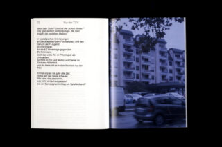 Ein Buch ist auf einer Doppelseite aufgeschlagen; die linke Seite enthält deutschen Text und die rechte Seite zeigt ein Foto von geparkten Autos vor einem mehrstöckigen Wohngebäude an einem bewölkten Tag.