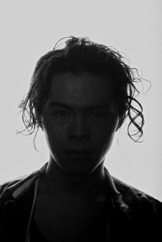 Die Silhouette einer Person mit welligem Haar ist vor einem hellen Hintergrund zu sehen, wobei die Gesichtszüge größtenteils im Schatten liegen.