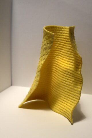 Ein einzelnes gelbes Reinigungstuch mit leicht gewellten Rändern steht aufrecht auf einer weißen Oberfläche.