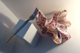 Eine silberne Gabel liegt auf einem weißen rechteckigen Block neben einer rosa-weißen Unterwäsche mit Leopardenmuster.