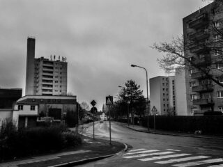 An einem bewölkten Tag schlängelt sich eine verlassene Stadtstraße zwischen mehreren mittelhohen Wohnhäusern hindurch.