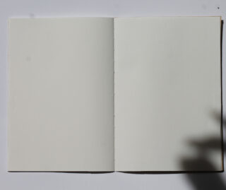 Ein offenes, leeres Notizbuch mit weißen Seiten von oben betrachtet; in der unteren rechten Ecke erscheint ein Schatten.