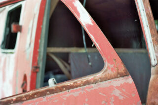 Nahaufnahme eines verrosteten, verwitterten roten Autos mit abblätternder Farbe, mit offener Tür und einem Teil des Innenrahmens.