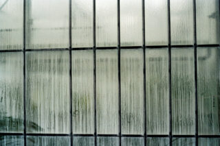 Vertikale und horizontale Gitterstäbe rahmen ein Fenster mit Kondenswasser und Feuchtigkeitsstreifen ein, wodurch die Sicht auf das, was sich hinter dem Glas befindet, verschwommen wird.