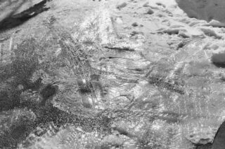 Reifenspuren und Fußabdrücke sind im matschigen, teilweise geschmolzenen Schnee auf einer sonnenbeschienenen Oberfläche sichtbar.