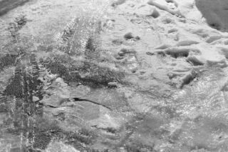 Nahaufnahme einer vereisten Fahrbahn mit Schnee und sichtbaren Reifen- und Schuhabdrücken auf der Oberfläche.