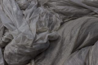 Nahaufnahme von zerknittertem, halbtransparentem grauem Stoff und strukturiertem Material, die übereinander geschichtet sind.