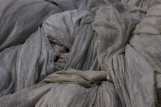 Eine Nahaufnahme mehrerer zerknitterter, heller Stoffbahnen mit einem strukturierten Rippenmuster.