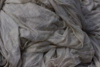 Nahaufnahme eines locker gestapelten, hellgrauen Stoffes mit einem transparenten, strukturierten und leicht zerknitterten Aussehen.