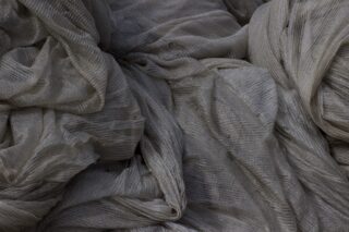 Nahaufnahme eines locker gestapelten, hellgrauen, durchscheinenden Stoffes mit sichtbarer Textur und Falten.