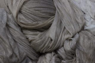 Eine Nahaufnahme eines mehrlagigen, zerknitterten hellgrauen Netzgewebes mit einer dezenten Streifenstruktur.