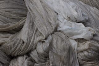 Eine Nahaufnahme von locker gefalteten und überlappenden hellgrauen und weißen Netzen oder Stoffen mit strukturierter Oberfläche.