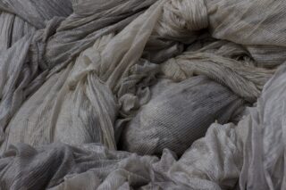 Eine Nahaufnahme eines locker gestapelten, strukturierten, hellgrauen Stoffes mit sichtbaren Falten und Knicken.